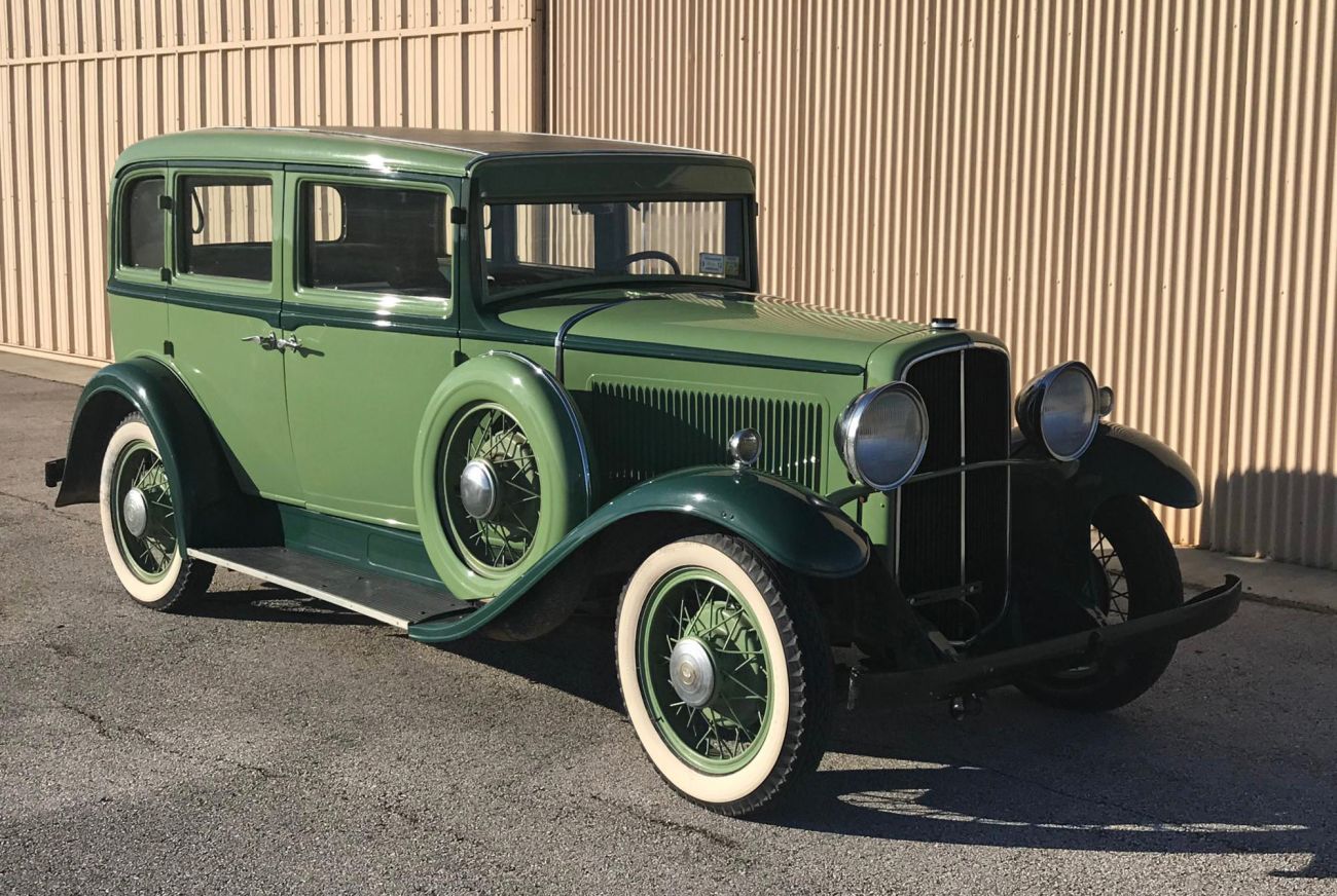 two-tone green 1932 nash car sitting in front of a hangar