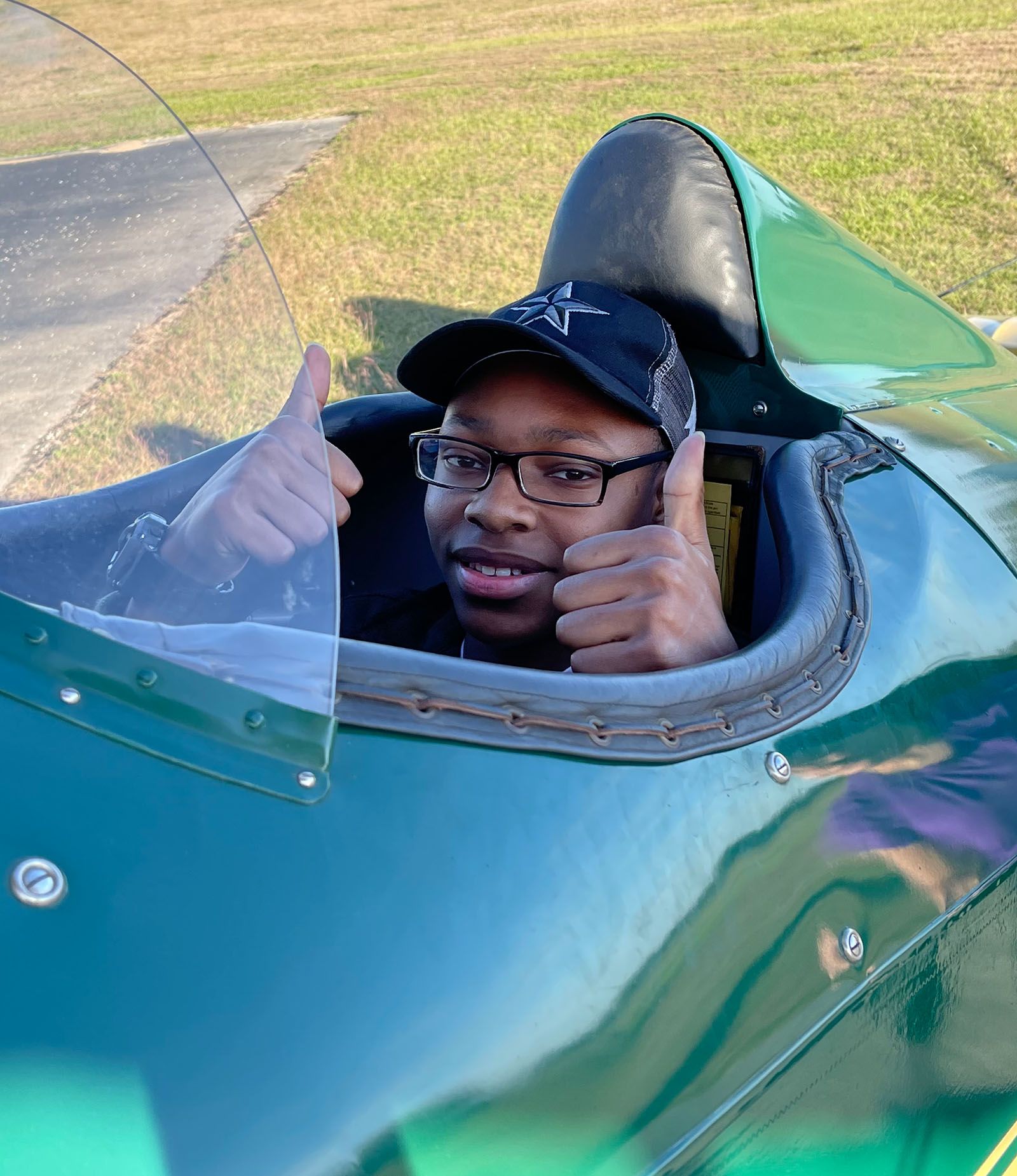 young man wearing headset in front seat of piper cub, turning around and smiling