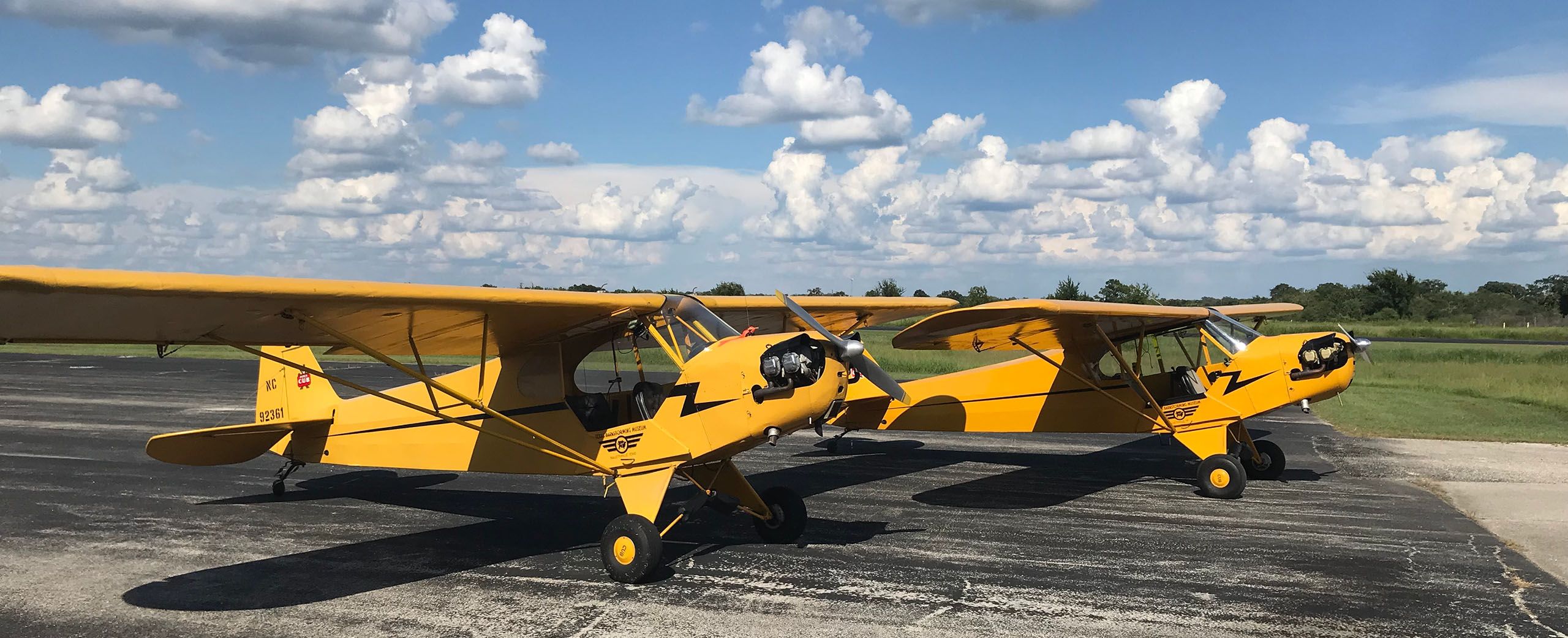 two yellow and black piper cub airplanes side by side on the taxiway