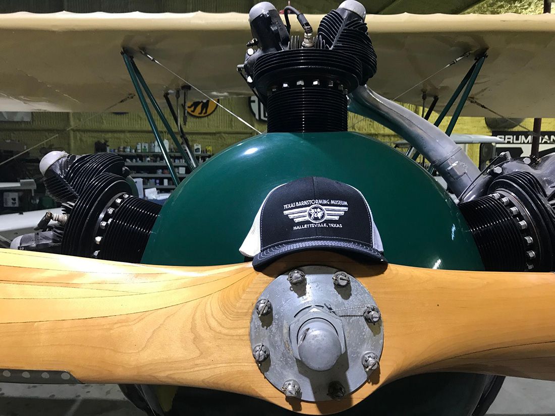 baseball cap resting on propeller. cap has a black front with white logo and white mesh sides.