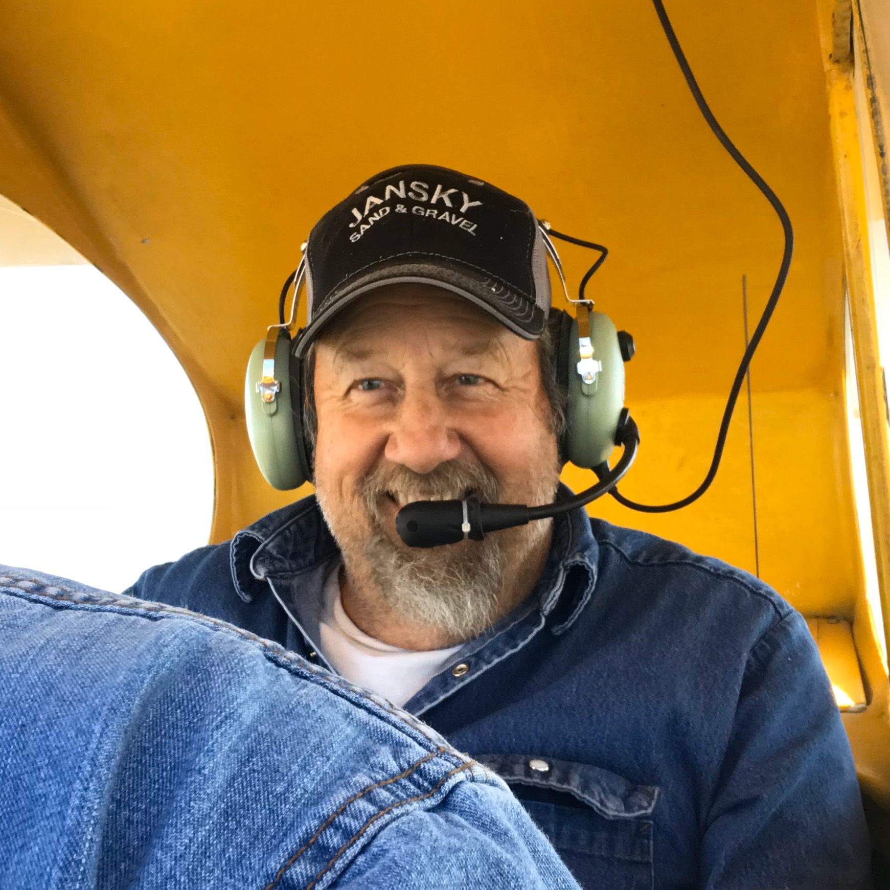 Mike Jansky in the back of a yellow Piper Cub, wearing headset and grinning ear-to-ear