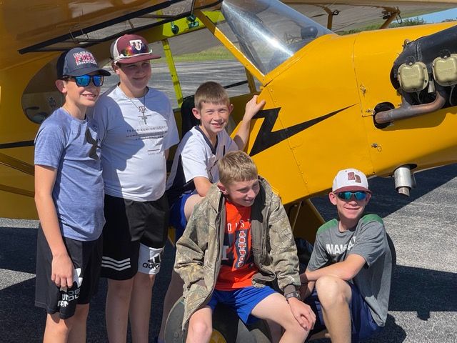 john cournoyer in blue shirt and brown felt fedora in front of a red biplane with yellow wings