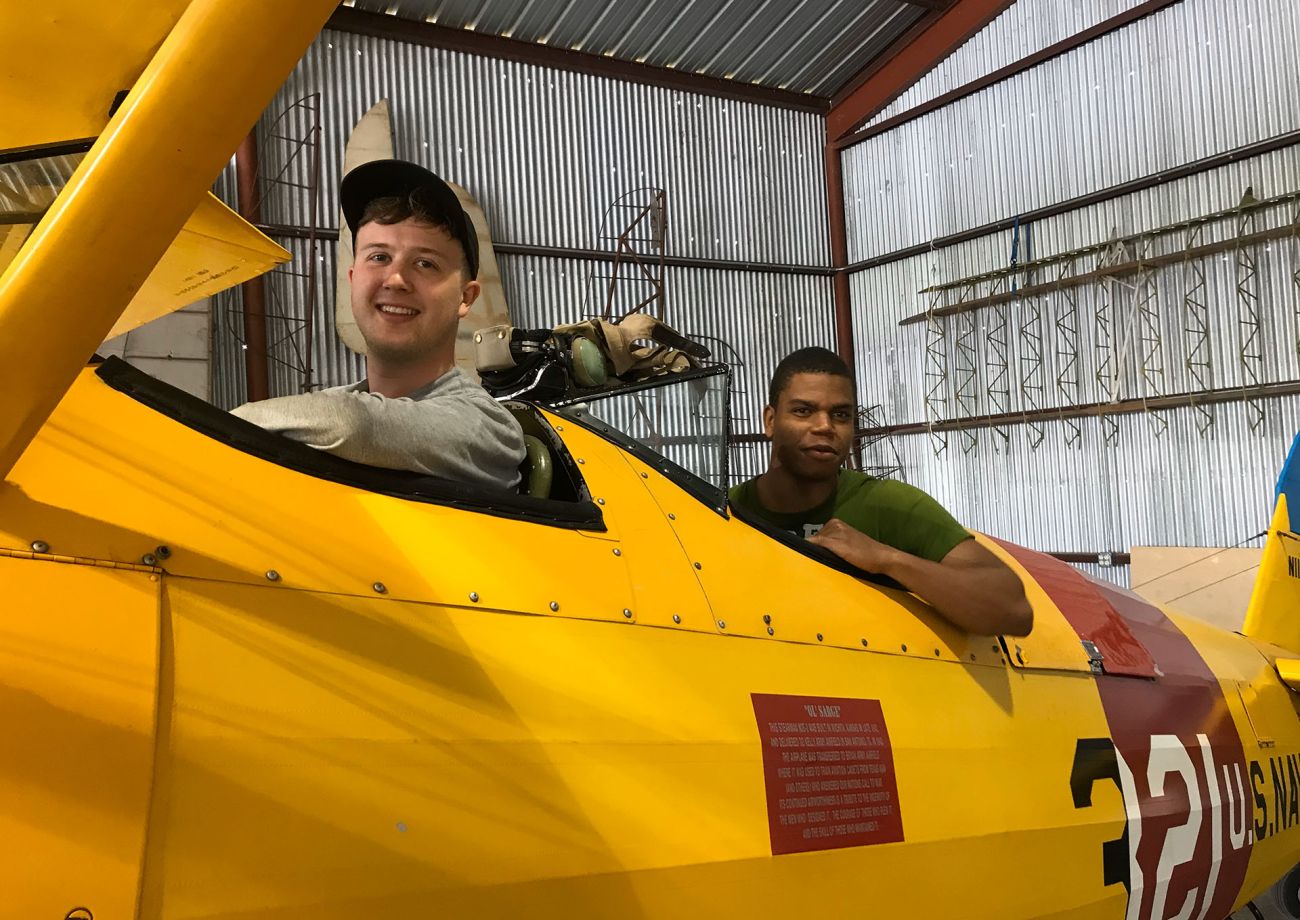 two young men sitting in an open cockpit of an antique navy biplane